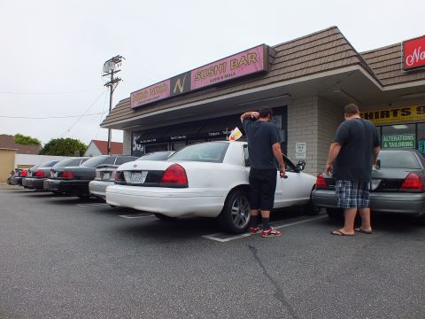 2003 Ford Crown Victoria - Photo of a white Ford Crown Victoria parked in a strip-mall lot beside a sushi bar, with two men at the trunk.