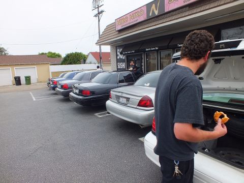 2003 Ford Crown Victoria - Photo of several parked Crown Victorias outside a sushi restaurant, with a bearded man standing at an open trunk.