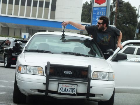 2003 Ford Crown Victoria - Photo of a man mounting a camera atop a white Ford Crown Victoria with push bar at a gas station.