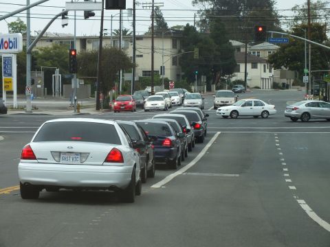 2003 Ford Crown Victoria - Photo of a white Crown Victoria with GHST VIC plate leading traffic at an intersection near a Mobil gas station.