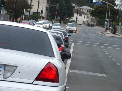 2003 Ford Crown Victoria - Photo of a white Crown Victoria leading cars and a motorcycle along a curving residential street.