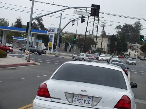 2003 Ford Crown Victoria - Photo of the rear of a white Crown Victoria with GHST VIC plate stopped at an intersection near a Mobil station.