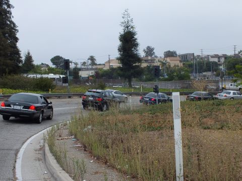 2003 Ford Crown Victoria - Photo of a black Crown Victoria rounding a freeway ramp curve beside an overgrown grassy median.