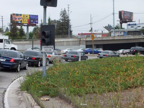 2003 Ford Crown Victoria - Photo of cars stopped at a signalized freeway on-ramp with billboards and a grassy median.