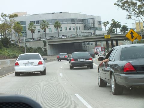 2003 Ford Crown Victoria - Photo of Crown Victorias on a curving freeway past a building, a driver gesturing from the window.