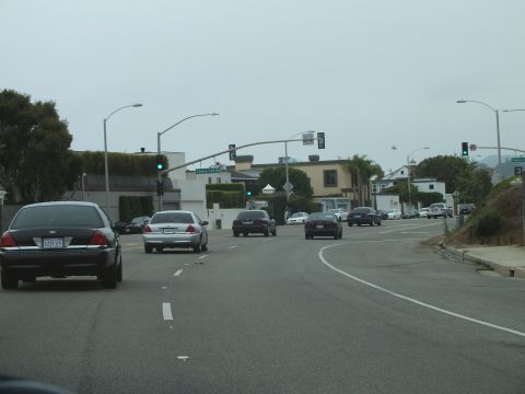 2003 Ford Crown Victoria - Driving photo of traffic on a coastal multi-lane road with traffic signals and a green street sign, not a technical document.