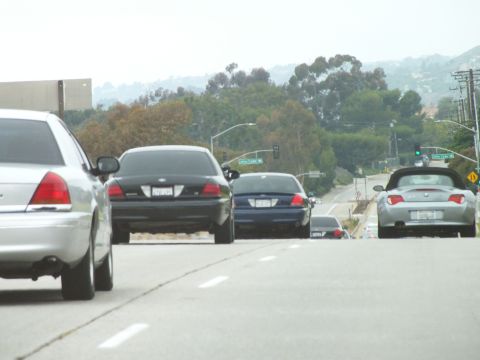 2003 Ford Crown Victoria - Road photo of cars and a roadster on a highway with hills in the background, not a technical document.