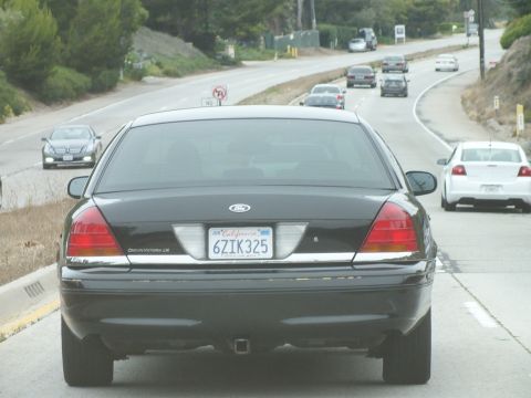 2003 Ford Crown Victoria - Road photo of a black Ford Crown Victoria rear with a California license plate on a curving highway, not a technical document.