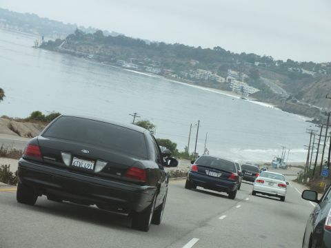 2003 Ford Crown Victoria - Road photo of a black Ford and other cars on a coastal highway above the shore, not a technical document.