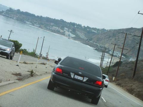 2003 Ford Crown Victoria - Road photo of a black Ford on a coastal highway overlooking a bay, not a technical document.