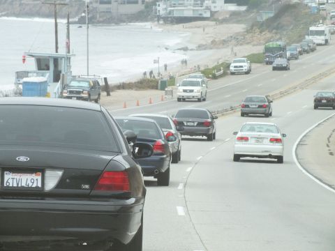 2003 Ford Crown Victoria - Road photo of a black Ford in coastal beach traffic with parked cars, not a technical document.