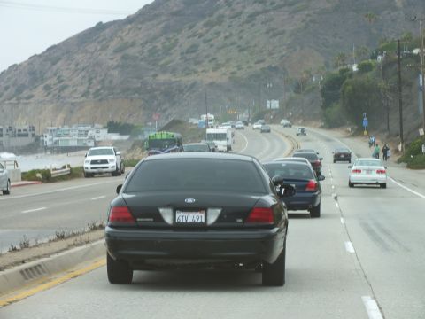 2003 Ford Crown Victoria - Photograph of a black Ford Crown Victoria sedan driving on a multi-lane coastal highway, not a technical document.