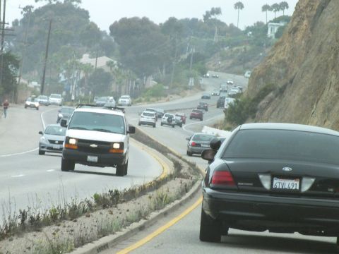 2003 Ford Crown Victoria - Photograph of cars including a Crown Victoria and a Chevrolet van on a curving coastal road, not a technical document.
