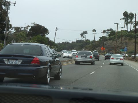 2003 Ford Crown Victoria - Photograph of a black Crown Victoria with a vanity plate driving on a coastal highway, not a technical document.