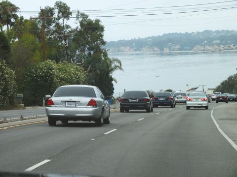 2003 Ford Crown Victoria - Photograph of a silver Crown Victoria leading cars on an ocean-view coastal highway, not a technical document.