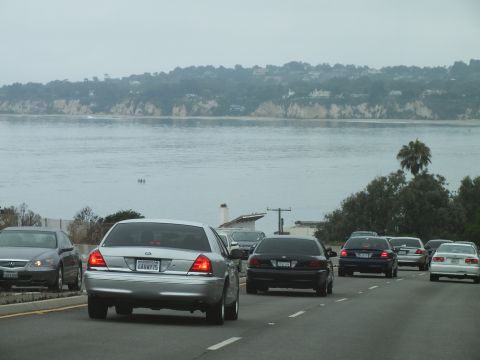 2003 Ford Crown Victoria - Photograph of a silver Crown Victoria amid traffic on a coastal highway above a bay, not a technical document.