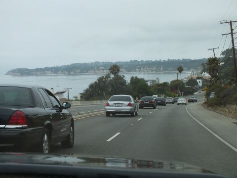 2003 Ford Crown Victoria - Photograph of a black sedan and traffic on a coastal highway above a hazy bay, not a technical document.