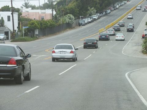 2003 Ford Crown Victoria - silver Ford Crown Victoria and dark sedans drive a multi-lane road separated by yellow barrier posts.