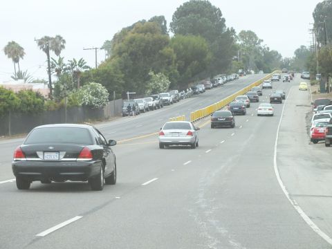 2003 Ford Crown Victoria - Photograph of a black Crown Victoria and silver sedan on a wide multi-lane coastal highway, not a technical document.