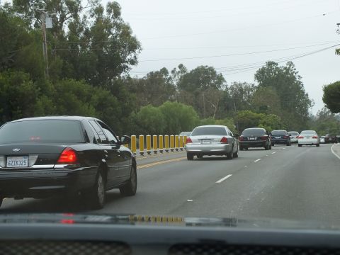 2003 Ford Crown Victoria - black Ford Crown Victoria drives in the foreground as silver and dark sedans follow on a tree-lined road.