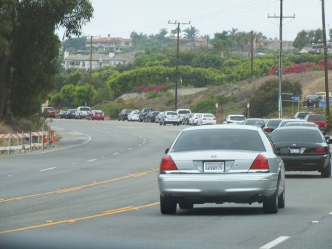 2003 Ford Crown Victoria - Photograph of a silver Crown Victoria on a curving coastal highway below hillside homes, not a technical document.