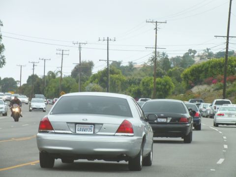2003 Ford Crown Victoria - Photograph of a silver Crown Victoria, black sedan and motorcyclist on a coastal highway, not a technical document.