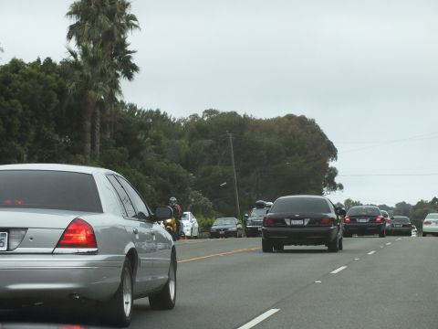 2003 Ford Crown Victoria - Photograph of a silver Crown Victoria, black sedan and motorcyclist in coastal highway traffic, not a technical document.