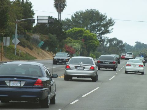 2003 Ford Crown Victoria - Photograph of a blue Crown Victoria with a vanity plate and other sedans on a coastal highway, not a technical document.