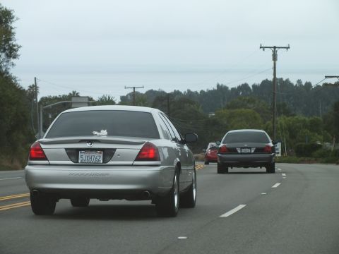 2003 Ford Crown Victoria - Photograph of a silver Marauder leading a sedan on a coastal highway, not a technical document.
