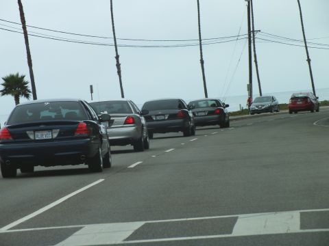 2003 Ford Crown Victoria - Photograph of sedans driving along a coastal road by the ocean, not a technical document.