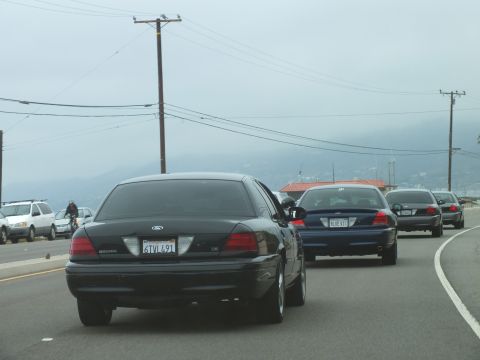 2003 Ford Crown Victoria - Photograph of a black Crown Victoria and sedans on a foggy coastal road, not a technical document.