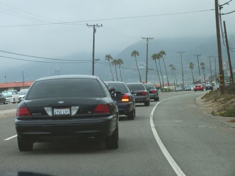 2003 Ford Crown Victoria - Photograph of a black Ford Crown Victoria leading a line of cars on a foggy coastal highway, not a technical document.