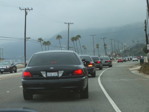 2003 Ford Crown Victoria - Photograph of a black Ford sedan following traffic on a misty coastal road during a car cruise, not a technical document.