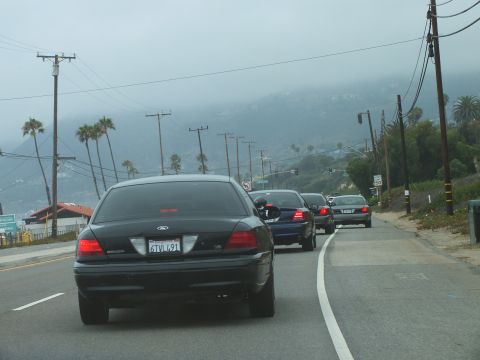 2003 Ford Crown Victoria - Photograph of a black Crown Victoria and other cars on a coastal highway curve, not a technical document.