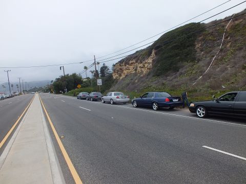 2003 Ford Crown Victoria - Photograph of several sedans parked along a coastal road shoulder beneath a bluff, not a technical document.