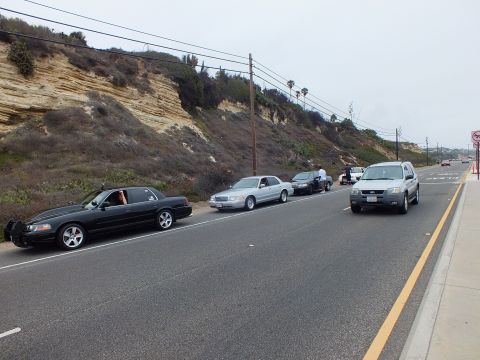 2003 Ford Crown Victoria - Photograph of cars and an SUV parked along a coastal highway near a hillside, not a technical document.
