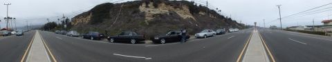 2003 Ford Crown Victoria - Wide panoramic photograph of a roadside car meetup with parked sedans and people, not a technical document.