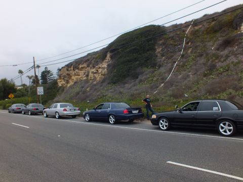 2003 Ford Crown Victoria - Photograph of several sedans parked along a coastal road with a person standing nearby, not a technical document.
