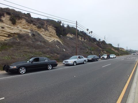 2003 Ford Crown Victoria - Photograph of sedans parked along a coastal road below a hillside with people gathered, not a technical document.