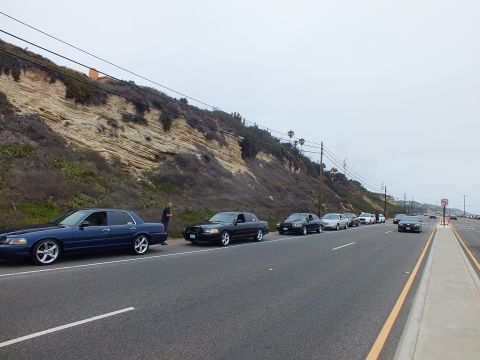 2003 Ford Crown Victoria - Photograph of blue and black sedans parked along a coastal highway near a bluff, not a technical document.