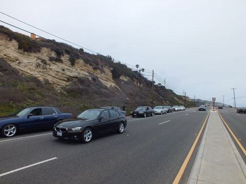 2003 Ford Crown Victoria - Photograph of a black wagon and sedans parked along a coastal highway near a hillside, not a technical document.