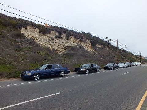 2003 Ford Crown Victoria - Photograph of a line of parked sedans along a coastal road beneath an eroded bluff, not a technical document.