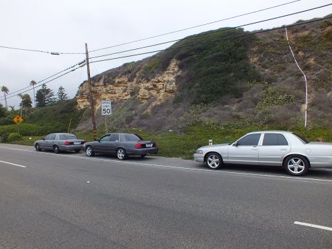 2003 Ford Crown Victoria - Photograph of silver and gray sedans parked along a coastal road by a bluff, not a technical document.