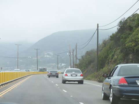 2003 Ford Crown Victoria - Photograph of sedans driving along a foggy coastal highway with mountains in the background, not a technical document.