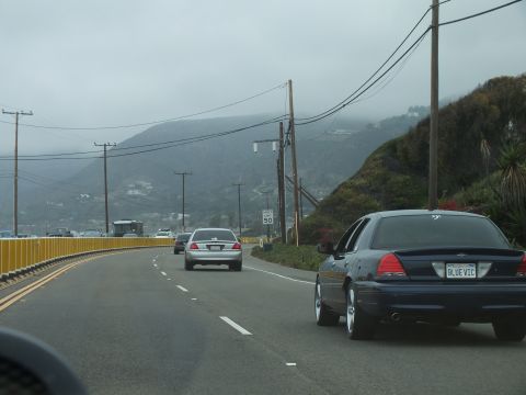 2003 Ford Crown Victoria - Photograph of a dark sedan following traffic on a foggy coastal highway, not a technical document.