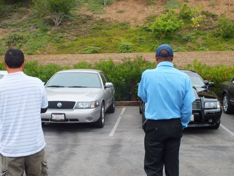 2003 Ford Crown Victoria - Photo of two men standing beside a silver Mercury sedan and a black car in a parking lot.