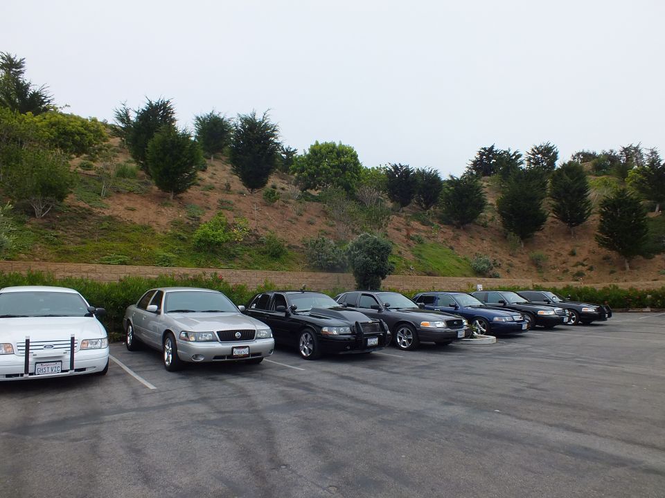 Parked sedans in a lot with a green hill behind