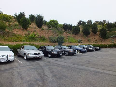 2003 Ford Crown Victoria - Photograph of several parked sedans in a lot in front of a hill, not a technical document.