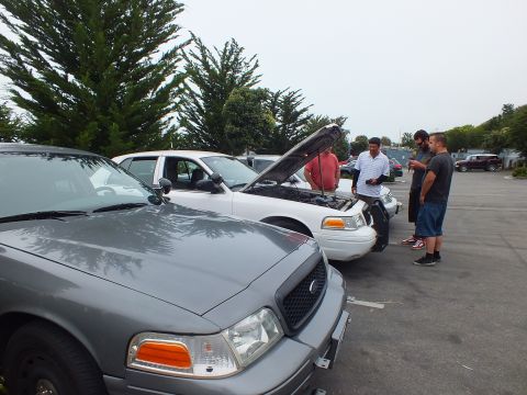 2003 Ford Crown Victoria - Photograph of people inspecting a white sedan with its hood up at a car meetup, not a technical document.