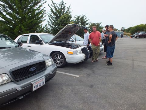 2003 Ford Crown Victoria - Photograph of people around a white sedan with its hood raised at a meetup, not a technical document.